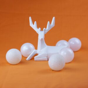 Minimalist white reindeer figurine surrounded by Christmas baubles on orange backdrop.